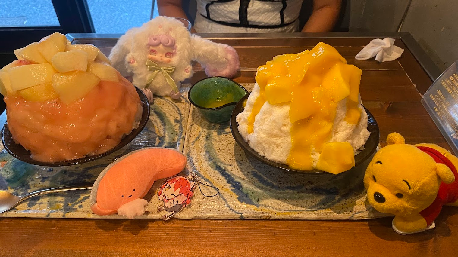 Photo of Two shaved iced desserts with plushie friends on the table.